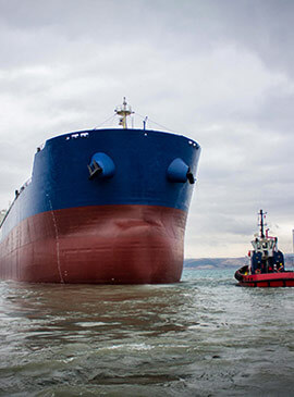 Barco de carga rojo con azul, siendo suministrado de combustible por barcaza de Enermar en alta mar