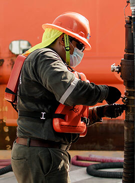 Colaborador de Enermar con casco naranja y traje especial de seguridad, cargando de combustible a buque a través de auto-tanque